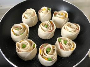 从一端叠起往另一端卷，末端蘸水粘住收口哦！平底锅放少许油烧热一次放入玫瑰锅贴煎1分钟（锅贴中间留一些距离）然后放入清水至最外层饺子皮一半的高度，盖上锅盖小火焖煮10分钟左右即可