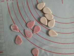 剩下的粉色面团取大概10克再揉入一点红曲粉，揉成红色色的面团，擀薄片用水滴状模具压出耳朵的形状来(没有模具的可以先压出一个圆来再呈米字切开或者取1克面团揉成水滴状在擀薄就是图中的样子了)