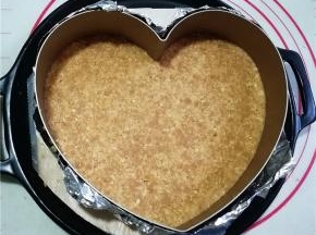 慕斯蛋糕圈底部用锡纸包裹住，放在烤盘中，将饼干碎倒入模具中，用勺子按压均匀后放入冰箱冷藏