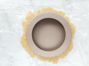 揭去上层的保鲜膜，将模具倒放在面皮上，再连同下层的保鲜膜倒扣过来，挞皮就铺到模具里。