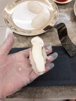 将拌好的米饭捏成饭团，上面放一片松茸，紫菜剪成长条裹在饭团上。