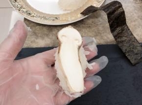 将拌好的米饭捏成饭团，上面放一片松茸，紫菜剪成长条裹在饭团上。