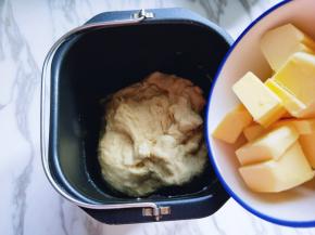 揉面15分钟后，加入提前室温软化的黄油。继续启动面包机揉面15分钟，这时面团已经有手套膜。