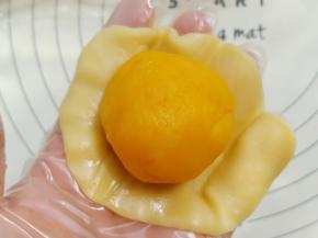 取一份月饼皮用手撑压扁，放入一枚金沙奶黄馅。
