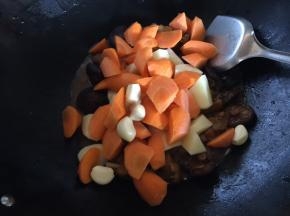 加入土豆、胡萝卜、蒜瓣翻炒后再盖锅盖继续焖至土豆和胡萝卜变软