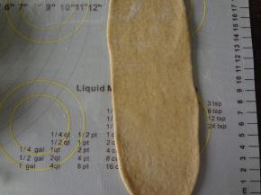 松弛好的面团擀成牛舌状，翻面横着放自上而下的卷起来