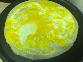 用煎饼果子工具戳破鸡蛋，使蛋黄和蛋清混合均匀铺满饼面。在鸡蛋液还没凝固时，撒入葱花、黑芝麻和盐、黑胡椒粉，火调到中火直到鸡蛋液基本凝固了再转回小火，不喜欢加的也可以省略掉这些调料。