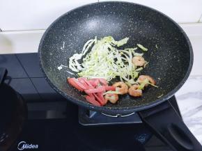 另起油锅，加入虾仁煸炒至变色，再加入卷心菜丝，火腿条，小火翻炒。