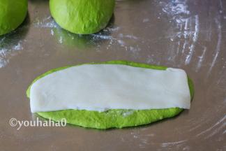 醒发后的面团用手拍扁，上下擀开成椭圆形，翻面后整理一下，取一份麻薯盖在面团上，麻薯比面团稍窄一点。