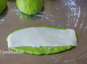 醒发后的面团用手拍扁，上下擀开成椭圆形，翻面后整理一下，取一份麻薯盖在面团上，麻薯比面团稍窄一点。