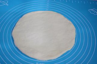 把面团取出按压排气，擀成跟披萨盘一样大小的圆形