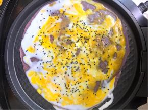 用刮板把鸡蛋均匀的刮散在饼皮表面，撒上适量的黑芝麻