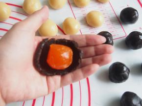 将红豆馅压扁放入蛋黄包起来，再取面团在手心压扁，放入红豆蛋黄馅，用虎口轻轻收口。