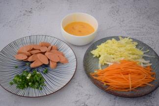 鸡蛋打散备用，火腿肠切片，白菜洗净切丝，胡萝卜去皮洗净切丝，葱切葱花