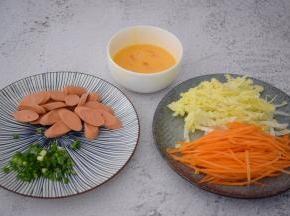 鸡蛋打散备用，火腿肠切片，白菜洗净切丝，胡萝卜去皮洗净切丝，葱切葱花
