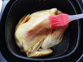 将腌制过的鸡放入空气炸锅中，刷一层玉米油在鸡身上。