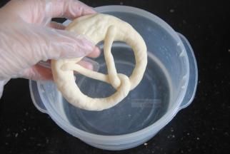 面团提前20分钟左右取出，先配备好碱水，把碱倒入水内，轻轻搅拌融化即可，带着手套抓起面团放入碱水，两面浸泡各20秒左右，捞出沥干水分放入垫有油布或油纸的烤盘里。