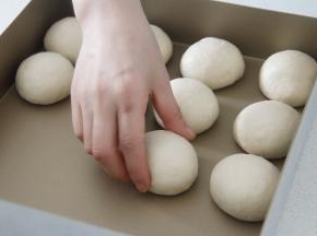静置好的面团再次收圆，排入方形烤盘中。