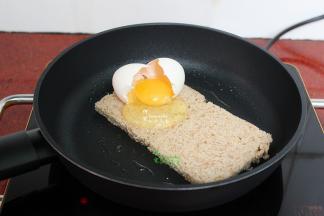 把吐司翻转之后，立刻把鸡蛋打入到吐司上面，接着用鸡蛋壳固定在吐司上，另外加一片吐司，防止鸡蛋液流到锅里。