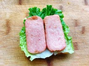 然后在吐司片上铺上一片生菜，再铺上两片煎香的午餐肉。放生菜的目的是为了搭配颜色，口感也更爽脆。