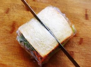 最后放上一片生菜，再用一片抹了法式沙拉酱的吐司片覆盖在表面，上面的吐司片和下面的吐司片要对称，尽量紧一些，四周低一些，中间高一些，然后用保鲜膜裹紧后，用面包刀对半切开。