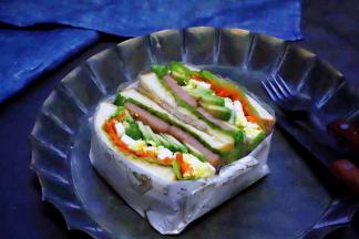 切成两半的三明治并排放在一起，然后用油纸叠成一个小纸盒，将三明治放在纸盒里，牛油果鸡蛋午餐肉三明治就做好了。