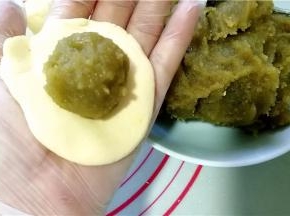取一面团，用手压成圆片后，放入绿豆沙馅。