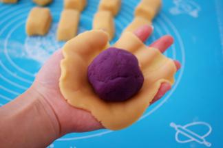 取一份饼皮，放在掌心按压成圆饼形，再放入紫薯馅