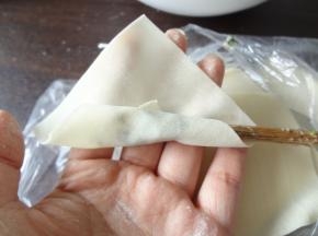 用筷子取一点馄饨馅放在馄饨皮上，将馄饨皮卷起，抽出筷子两端向中间捏合