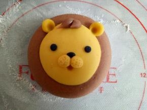 如图，将狮子的眼睛也做好，鼻子上用牙签扎一些小孔，用细一点的筷子扎出嘴巴来，适量可可面团做出狮子的鬃毛来(每个鬃毛大概0.5克)