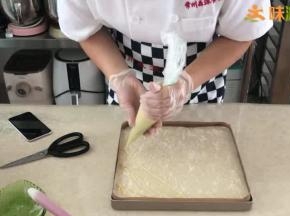 烤盘提前铺好油布或油纸，混合好的面糊倒入烤盘中用刮板刮平，表面撒上椰蓉，挤上香蕉卡士达酱。