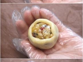 取一份饼皮揉圆后压扁成圆状，放入五仁馅，用虎口把饼皮慢慢向上推，最后揉搓至饼皮完全包裹住馅料，搓圆后排入垫油布的烤盘。