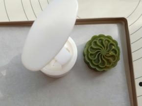 月饼模具撒点低粉，然后磕一下，把多余的粉磕出去，粉一定不要多。薄薄一层。把包好的桃山皮月饼放入模具中，然后在阳晨长方形牛扎糖烤盘上按出花纹。