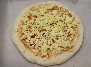 从冰箱取出饼皮，放上烤盘，抹上披萨酱，放上马苏里拉芝士碎