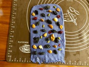 取小的蓝色面团，擀成和面包机内宽差不多的长方形，底边压薄，均匀的撒上黑加仑干、杏仁、每日坚果（里头包含多种坚果和干果）