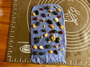 取小的蓝色面团，擀成和面包机内宽差不多的长方形，底边压薄，均匀的撒上黑加仑干、杏仁、每日坚果（里头包含多种坚果和干果）