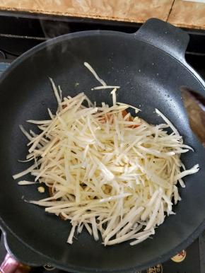 接着倒入沥水后的土豆丝，继续翻炒均匀。