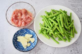 猪肉洗净切成薄片加入料酒、盐、味极鲜酱油、玉米淀粉、食用油抓匀腌制半小时，豇豆去掉头尾洗净切寸段，蒜切片