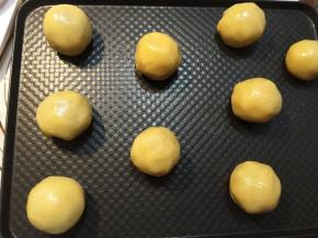 取出一个小剂子揉圆，压扁，中间放上一块馅料，包好捏紧，然后放到烤盘上。