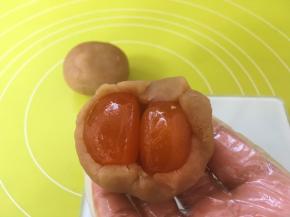 包裹上两颗咸蛋黄，用双手虎口部分，一点点推揉莲蓉馅，将咸蛋黄包裹好；