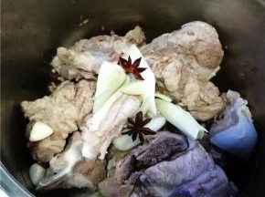将猪骨用温水洗净，放入电压力锅里，将葱姜、八角和调料包放入。