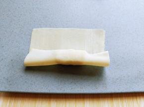 将馄饨皮的一端对折。再将另一端对折。