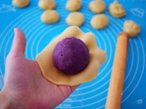 取一份饼皮，放在掌心按压成圆饼形，再放入紫薯蛋黄馅