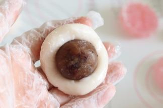 取一个冰皮面团，捏开，放入馅料，包好。