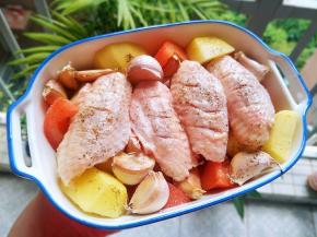 烤盘底下放入土豆番茄块。再铺上鸡翅，记住，不要在鸡翅上面放东西。等下考出来才会上面脆，下面嫩。鸡翅的边边角角可以塞东西。蒜头粒就塞边角上，鸡翅两面涂抹上橄榄油跟海盐，最后撒上些黑胡椒粉