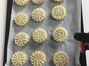 用喷雾瓶从高处薄薄的喷一层水雾在刚刚脱模好的月饼胚上，以免月饼在烤的过程中开裂！

