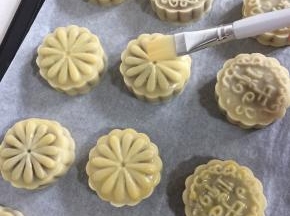 5分钟后出炉，绒毛刷先在碗壁上刮去多余的蛋液，再在月饼表面花纹上薄薄的刷一层蛋液。（鸡蛋加点水搅拌均匀后过筛，再刷蛋液就很均匀了。蛋液不要刷的太多，要不然蛋液多了月饼表面的花纹会模糊。）