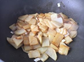 当留的炸虾底油油温4、5成热时，放入葱花姜片爆香，放入土豆片，放入1勺的酱油，翻炒均匀。