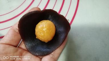 取一份豆沙用手按成圆片，放入一个蛋黄。