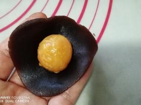 取一份豆沙用手按成圆片，放入一个蛋黄。